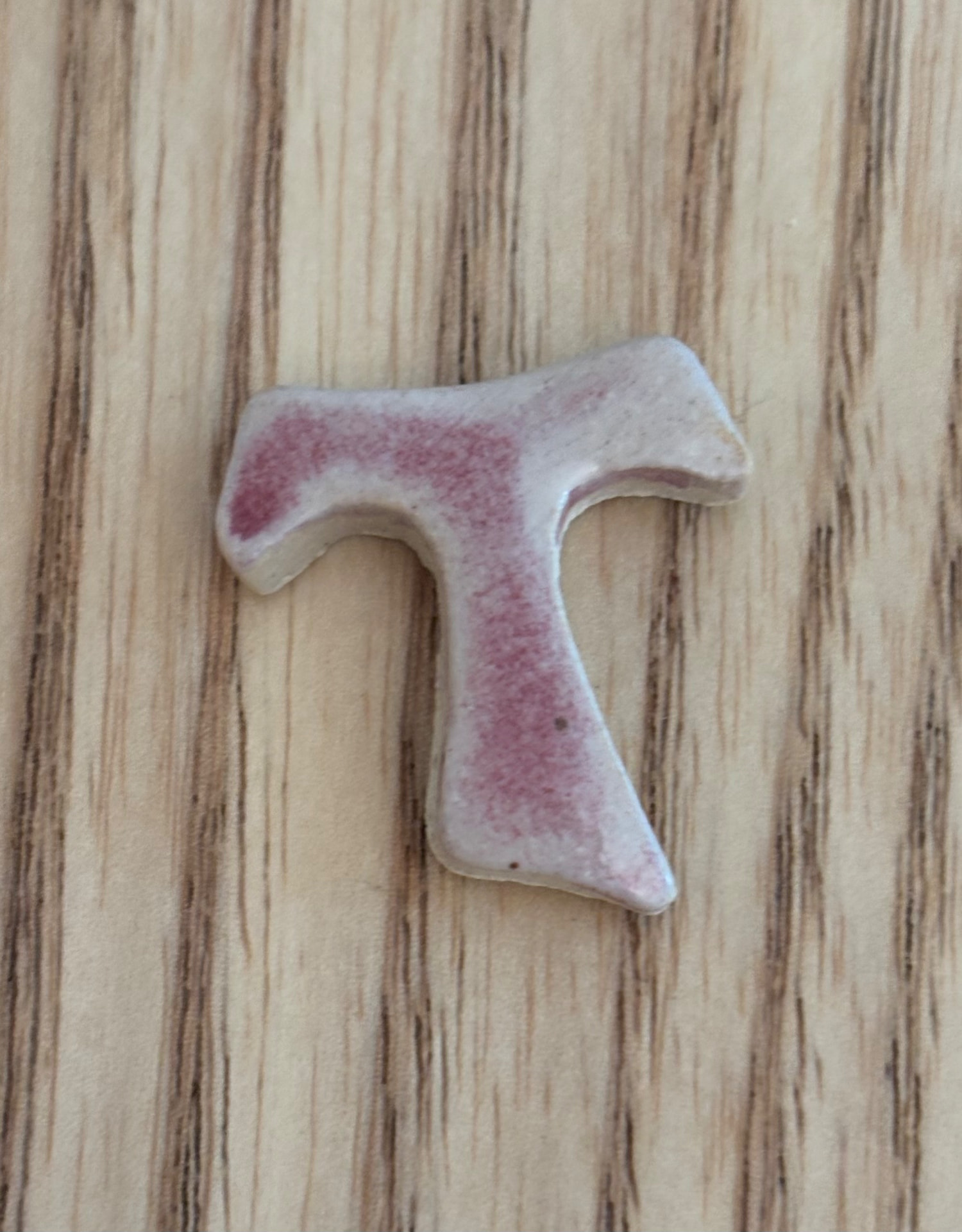 Pendentif en céramique en forme de Tau, blanc et rose, posé sur du bois strié