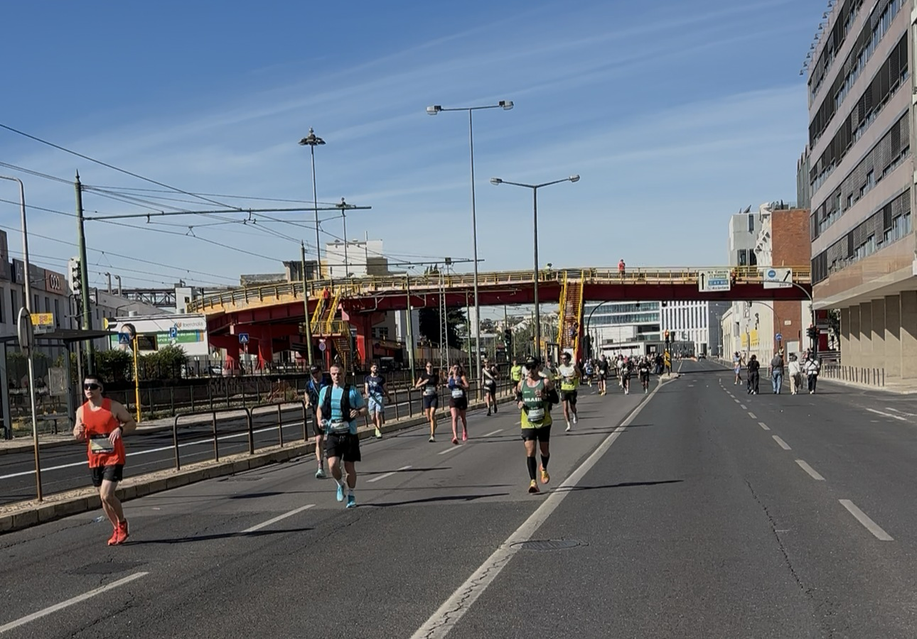 Runners on an avenue in Lisbon during the marathon, under a blue sky.
