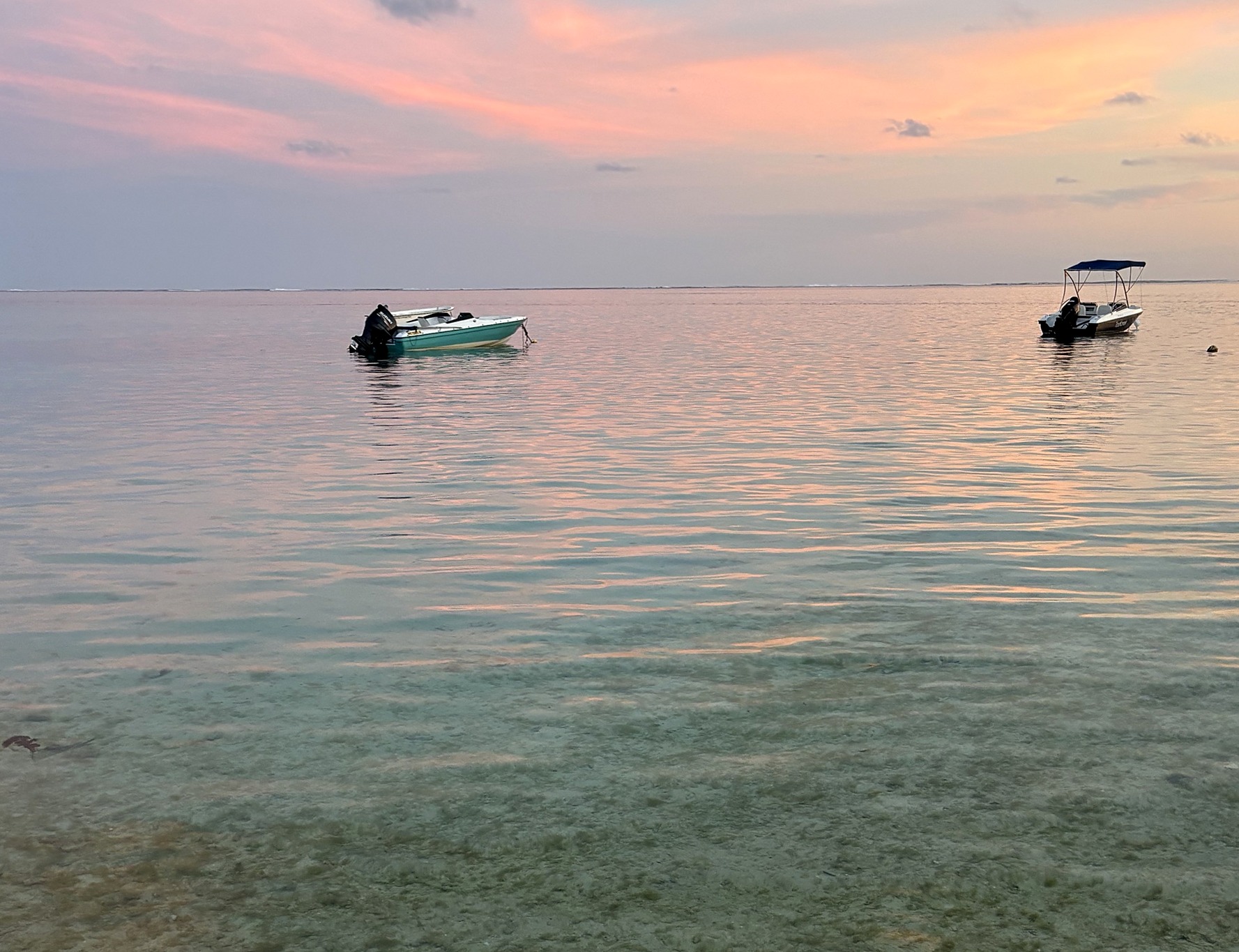 Mare calmo al tramonto, due piccole barche all'ancora e riflessi rosa sull'acqua